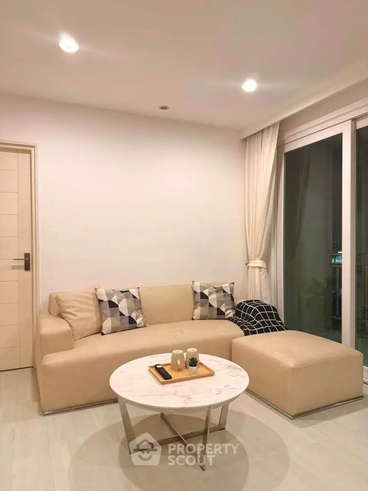 Modern living room with beige sofa and marble coffee table, featuring elegant decor and large windows.
