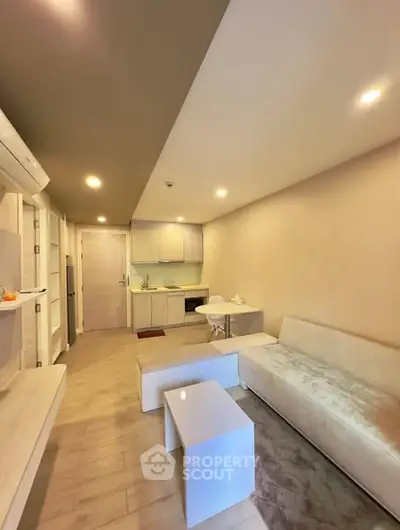 Modern living room with sleek kitchen in open layout, featuring minimalist furniture and warm lighting.