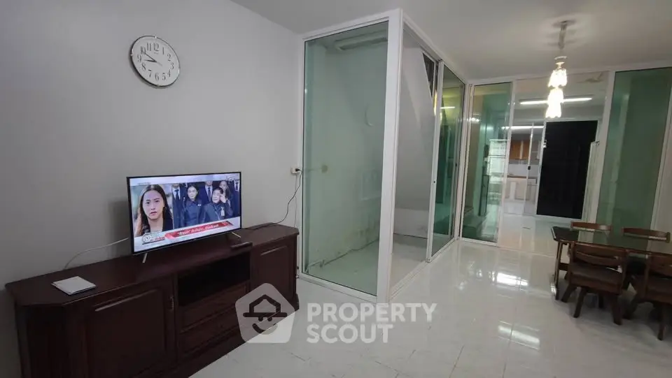 Spacious living room with modern TV setup and dining area, featuring glass partition and elegant lighting.