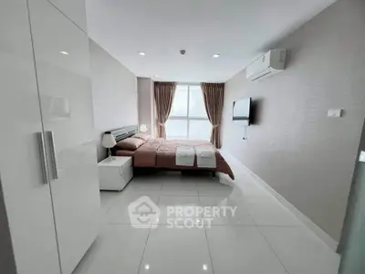 Modern bedroom with sleek design, featuring a large bed, wall-mounted TV, and ample natural light.
