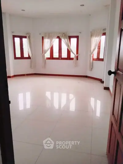 Spacious empty room with large windows and white tiled flooring, perfect for customization.