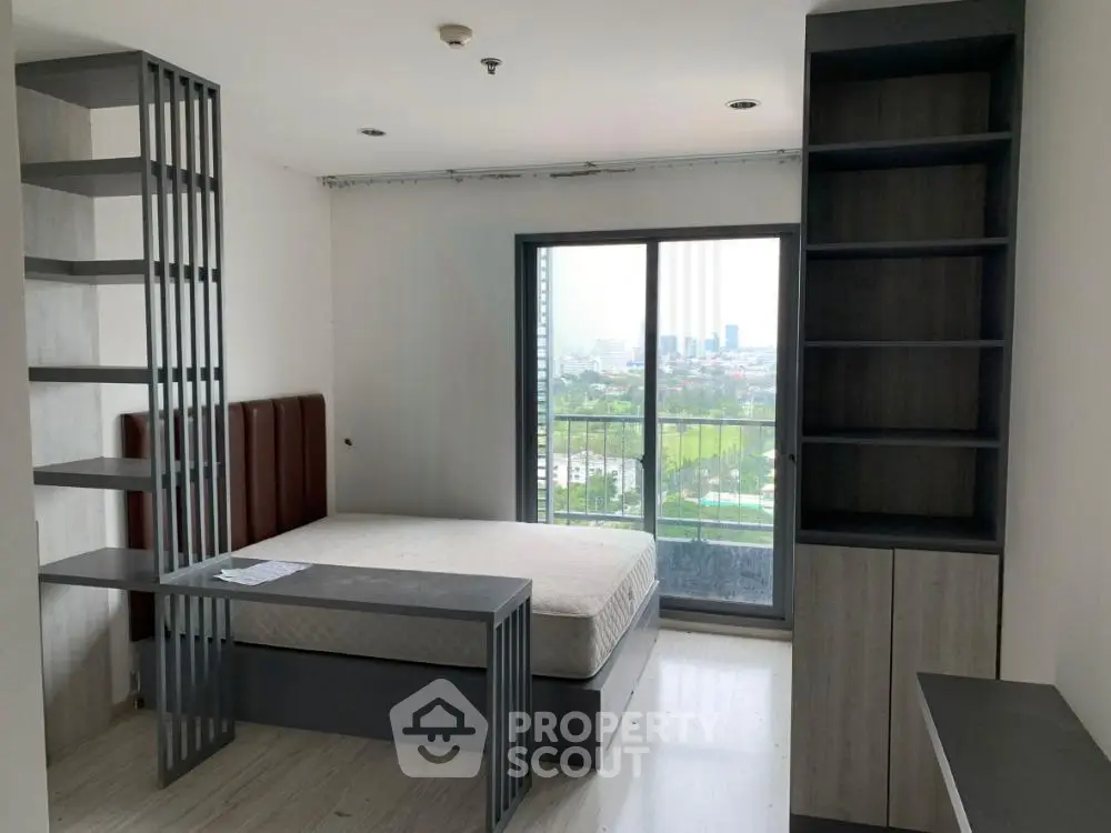 Modern bedroom with large window and city view, featuring sleek furniture and ample natural light.