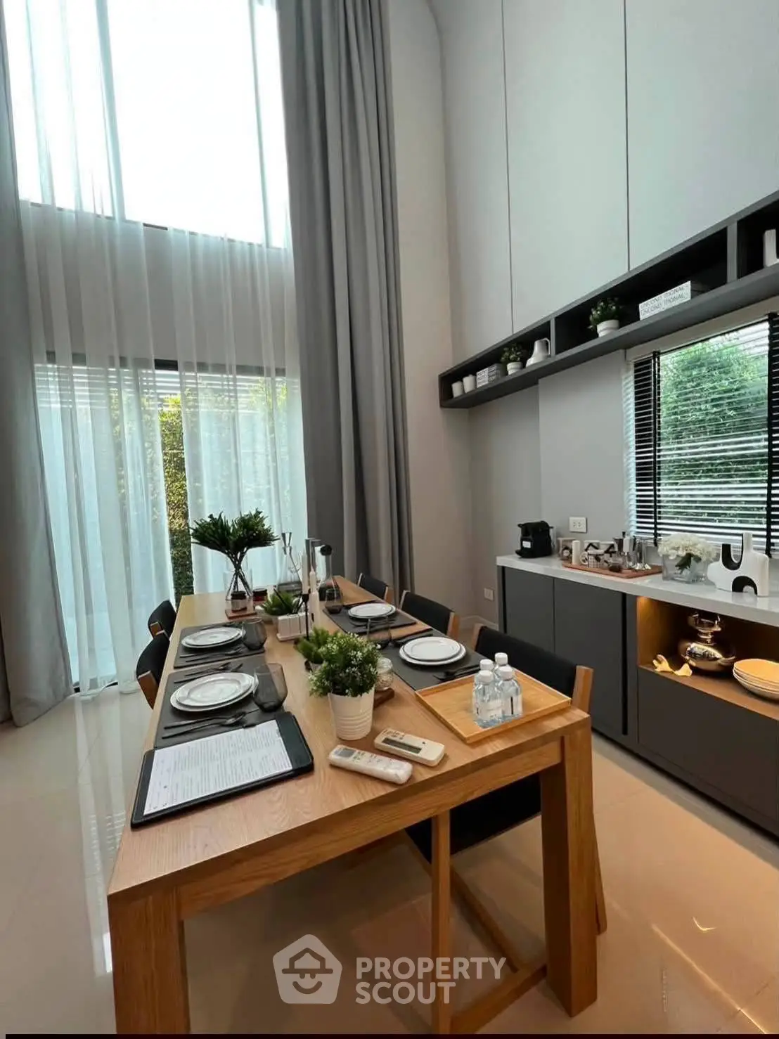 Elegant dining area with high ceilings and modern decor, featuring a stylish wooden table set for a meal.