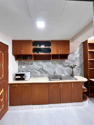 Charming kitchen with wooden cabinets and marble backsplash, featuring a microwave and elegant decor.