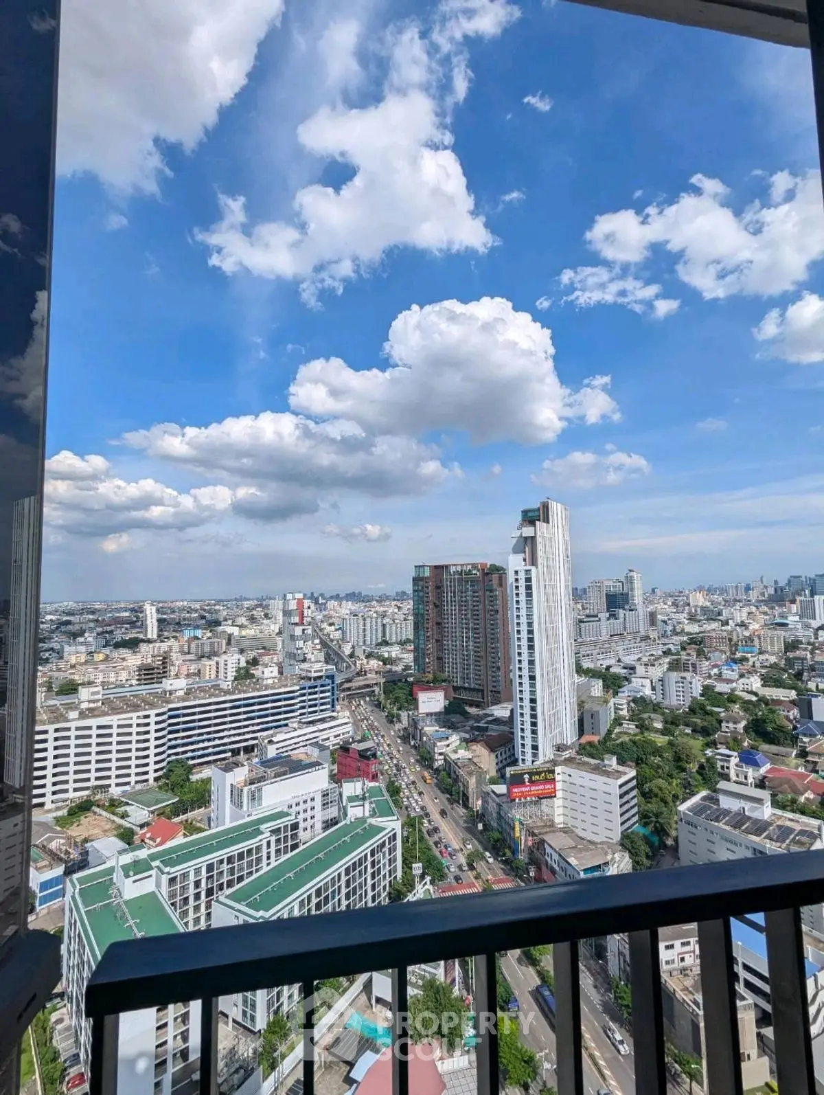 Stunning cityscape view from high-rise balcony with clear blue sky and clouds.