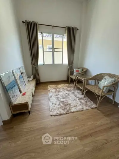 Cozy small living room with wooden flooring, wicker chairs, and a soft rug under natural light.