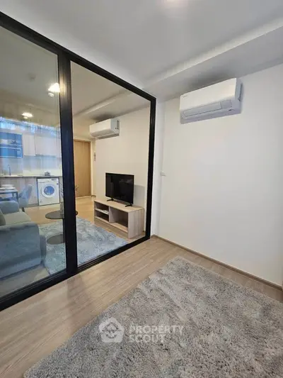 Modern living room with glass partition and air conditioning, featuring cozy carpet and sleek TV setup.