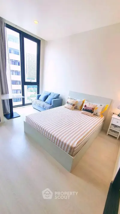 Bright and modern bedroom with large window and cozy seating area in a high-rise apartment.