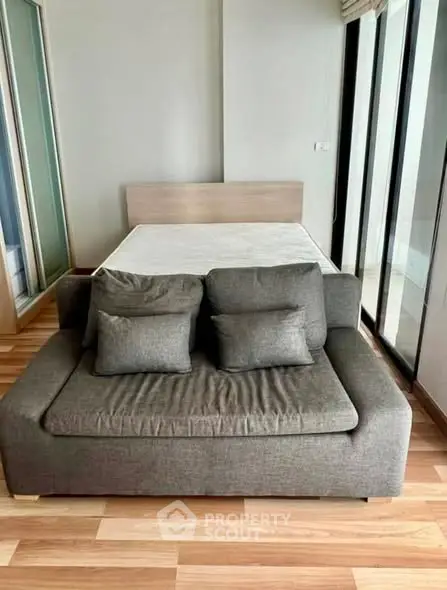 Modern studio apartment with stylish sofa and bed, featuring floor-to-ceiling windows for natural light.