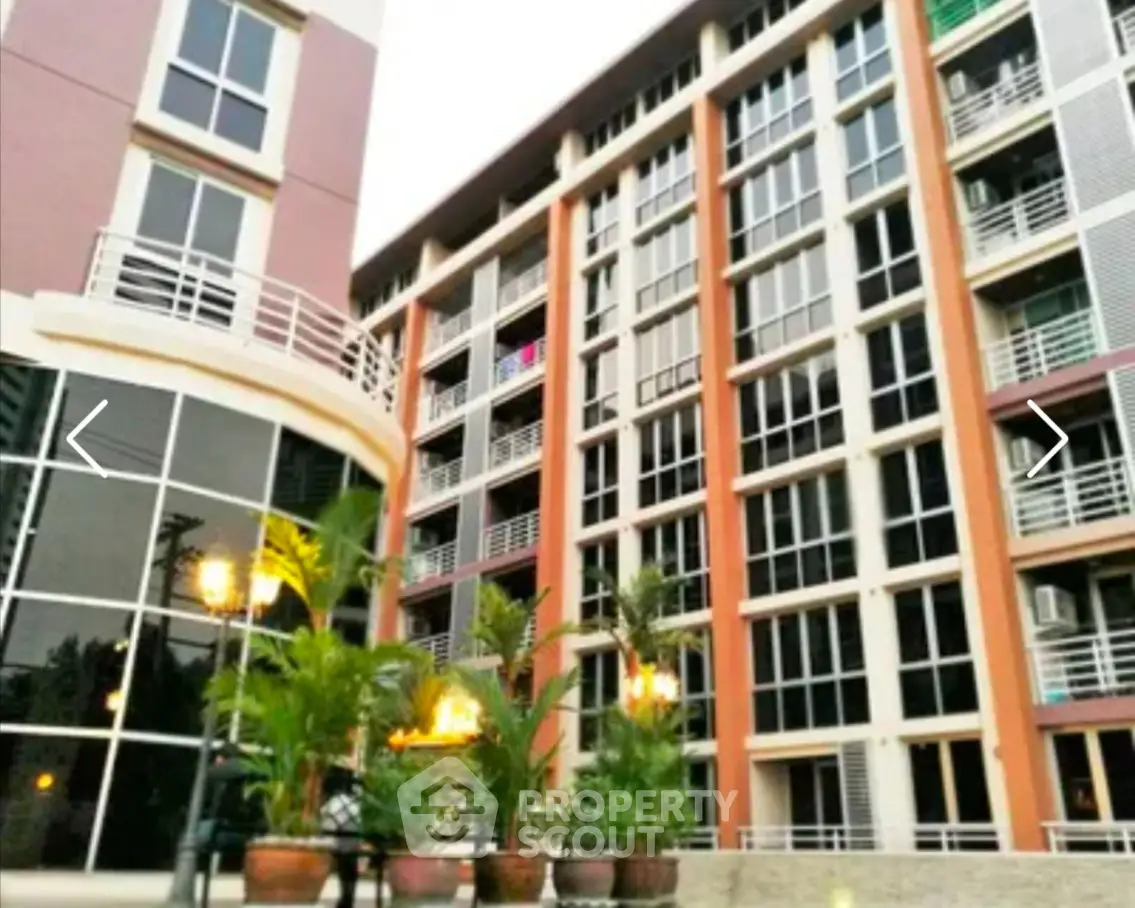 Modern multi-story apartment building with large windows and potted plants in the foreground.