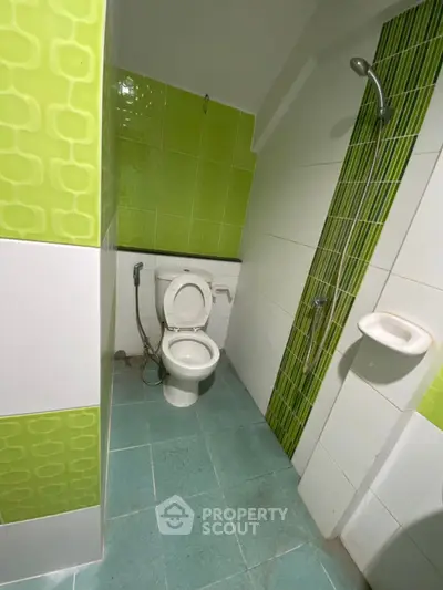 Compact bathroom with green tiles and shower area, ideal for small spaces.