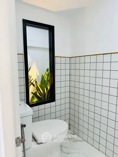 Modern bathroom with sleek white tiles and a stylish black-framed window.