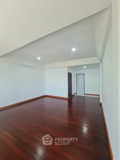 Spacious empty room with polished wooden floors and white walls, ideal for customization.