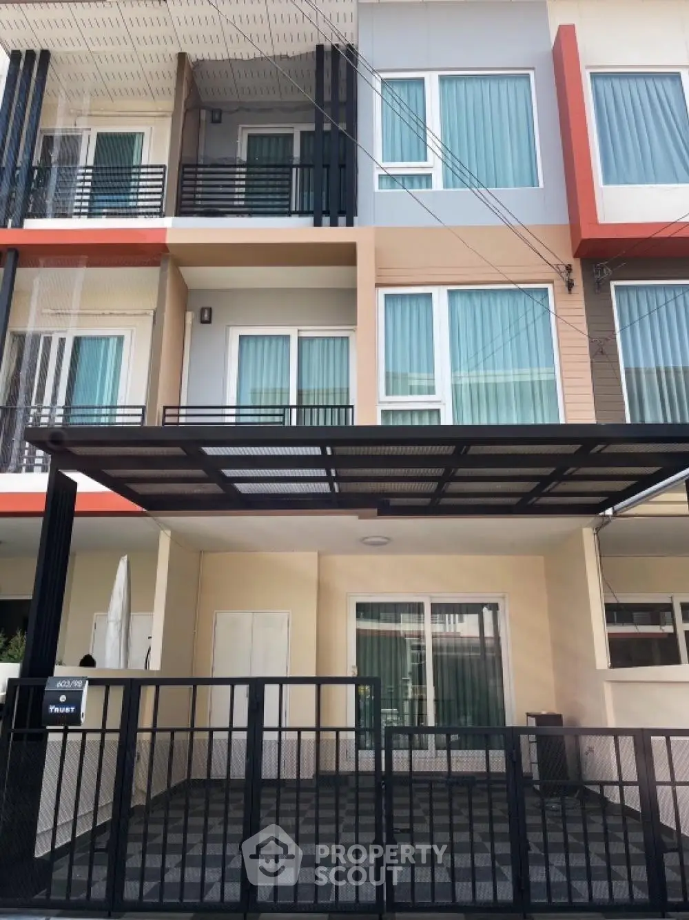 Modern townhouse with striking color accents, featuring a secure gated entrance and a shaded carport, ideal for urban living.
