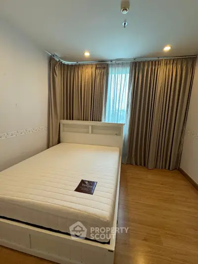 Cozy bedroom with wooden flooring and large window, featuring a comfortable bed and elegant curtains.