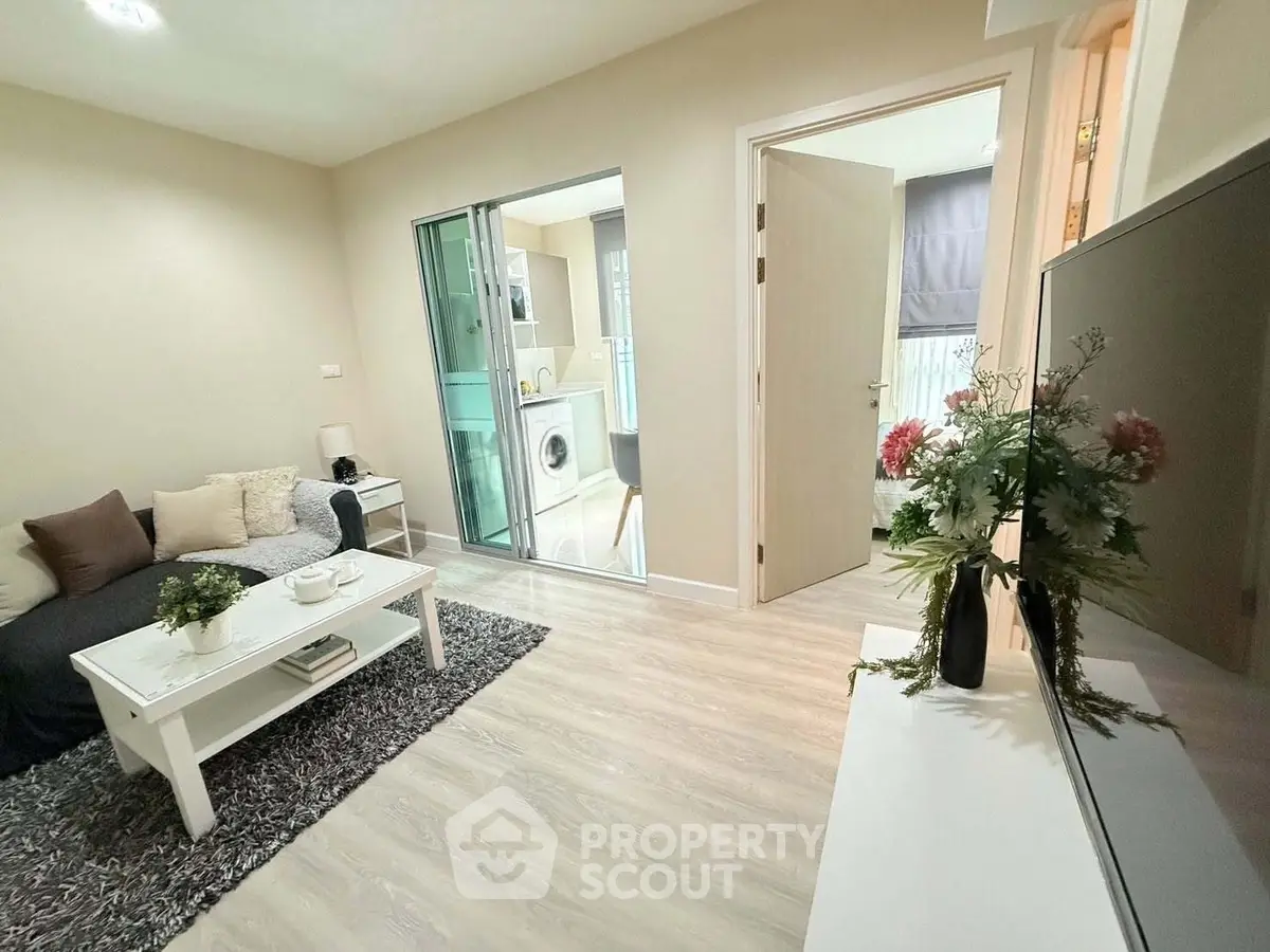 Modern living room with cozy decor and view into laundry area, featuring sleek furniture and stylish flooring.