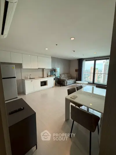 Modern open-layout living room with kitchen and city view, featuring sleek furniture and ample natural light.