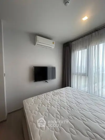 Modern bedroom with large window, air conditioning, and wall-mounted TV in a bright apartment.