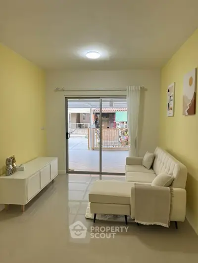 Bright living room with yellow walls, modern white sofa, and sliding glass doors leading to a balcony.
