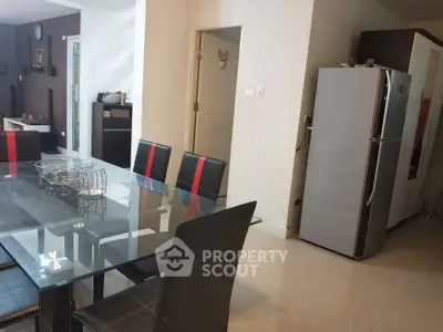 Modern dining area with glass table and sleek black chairs, adjacent to a spacious kitchen.