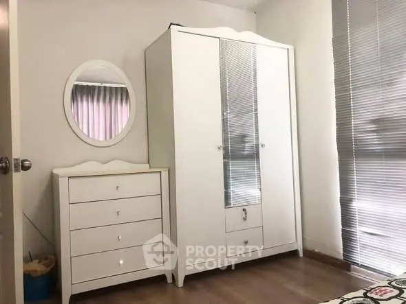 Cozy bedroom with white wardrobe and dresser, featuring a round mirror and blinds.