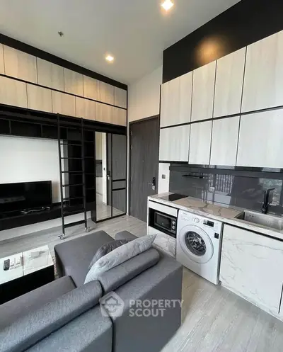 Modern living room with integrated kitchen and washing machine, featuring sleek cabinetry and cozy seating.