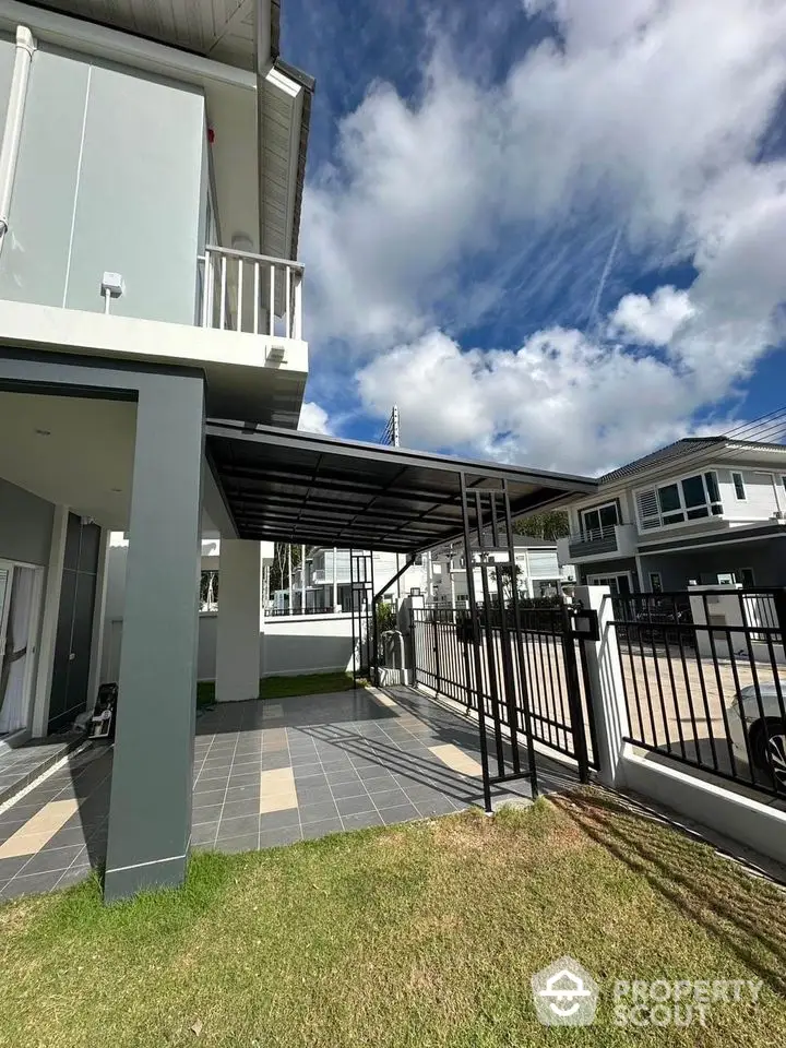 Modern house exterior with covered parking and lush green lawn under a bright blue sky.