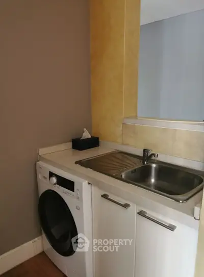Compact kitchen area with washing machine and sink, ideal for efficient living spaces.