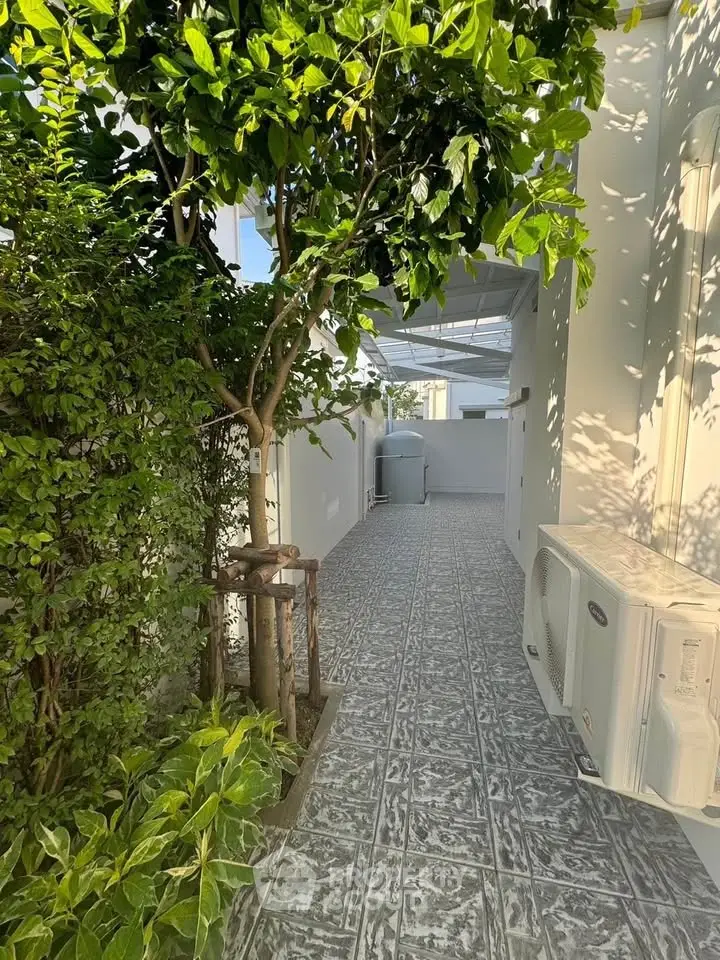 Charming outdoor corridor with lush greenery and modern air conditioning unit, perfect for serene living.