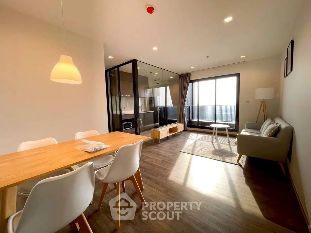 Modern living room with dining area and large windows, featuring stylish furniture and wooden flooring.