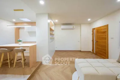 Modern open-plan living room with stylish kitchen and cozy seating area, featuring wooden accents and bright lighting.
