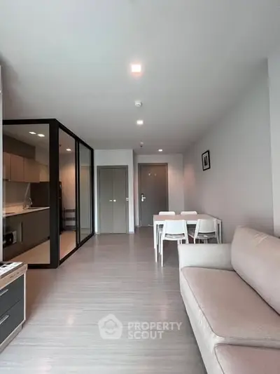 Modern open-plan living room with sleek kitchen and dining area, featuring contemporary furniture and neutral tones.