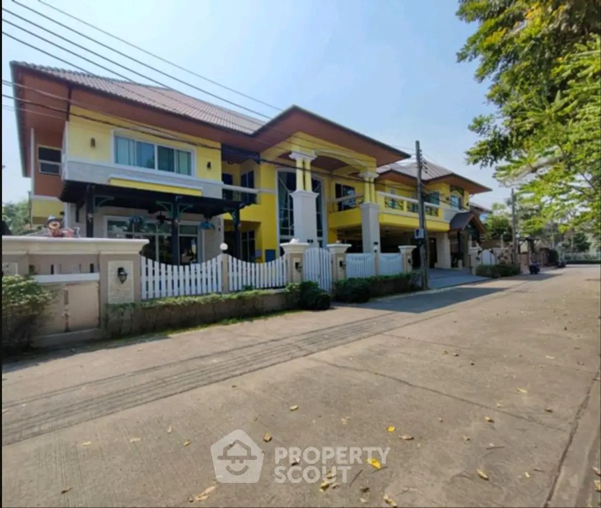 Spacious yellow two-story house with white picket fence and driveway in a serene neighborhood.