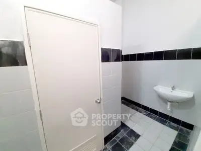 Compact bathroom with white and navy blue tiles, featuring a small wall-mounted sink and a mirrored medicine cabinet.