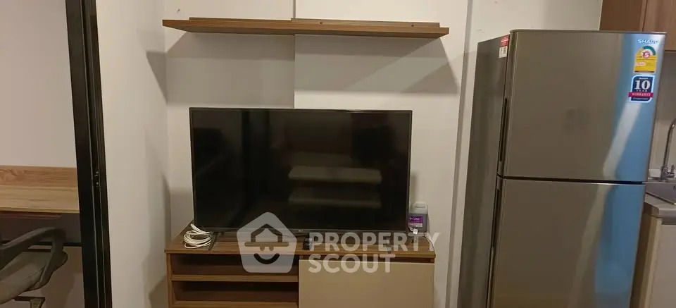 Modern apartment interior with TV, shelves, and stainless steel fridge in a cozy living space.