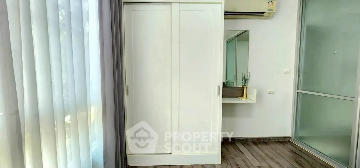 Modern bedroom with sleek wardrobe and air conditioning, featuring elegant flooring and natural light.