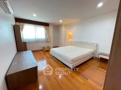 Spacious bedroom with wooden flooring and modern furnishings in a bright apartment.