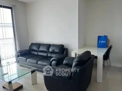 Modern living room with black leather sofas and glass coffee table in bright apartment.