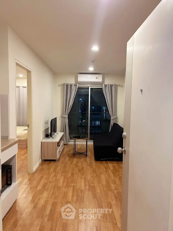 Modern living room with wooden flooring and balcony access, featuring a sleek TV setup.