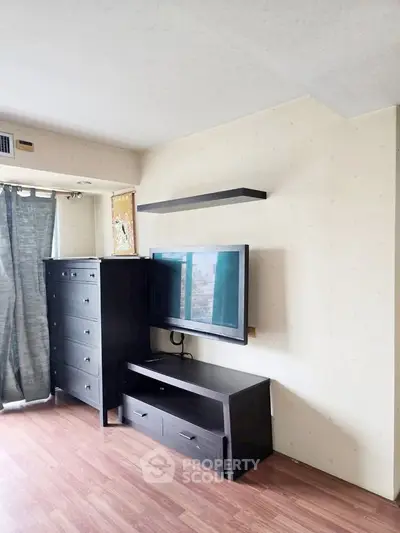 Modern living room with sleek black furniture and mounted TV, featuring hardwood floors and natural light.