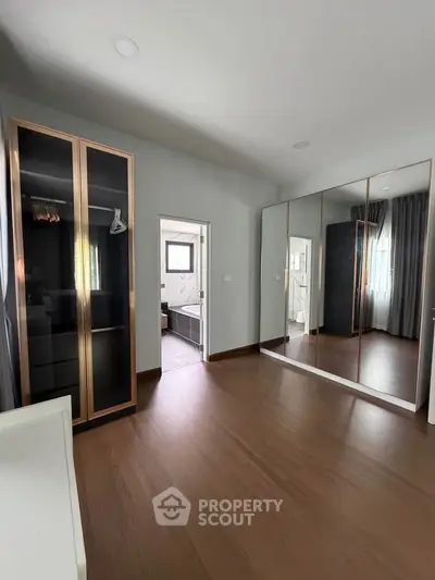 Spacious bedroom with elegant wooden flooring and mirrored wardrobe doors.