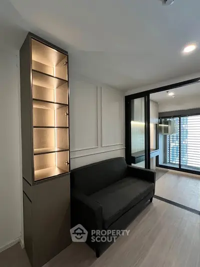 Modern living room with sleek black sofa and illuminated display cabinet, featuring large windows for natural light.