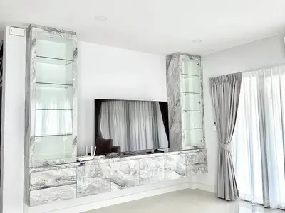 Modern living room with sleek marble cabinetry and large TV, featuring elegant curtains and bright natural light.