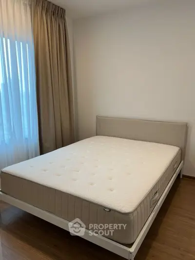 Spacious bedroom with natural light and elegant curtains, featuring a comfortable bed and wooden flooring.
