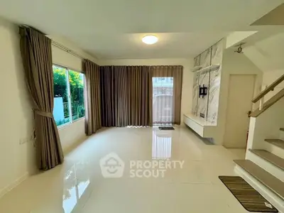 Spacious living room with large windows and elegant curtains, featuring a modern staircase and sleek flooring.