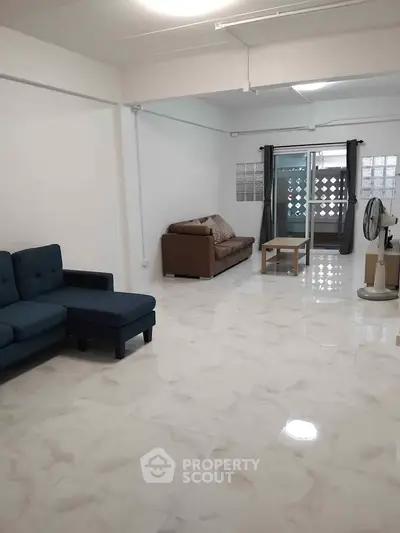 Spacious living room with modern furniture and marble flooring, featuring a cozy sofa and natural light.