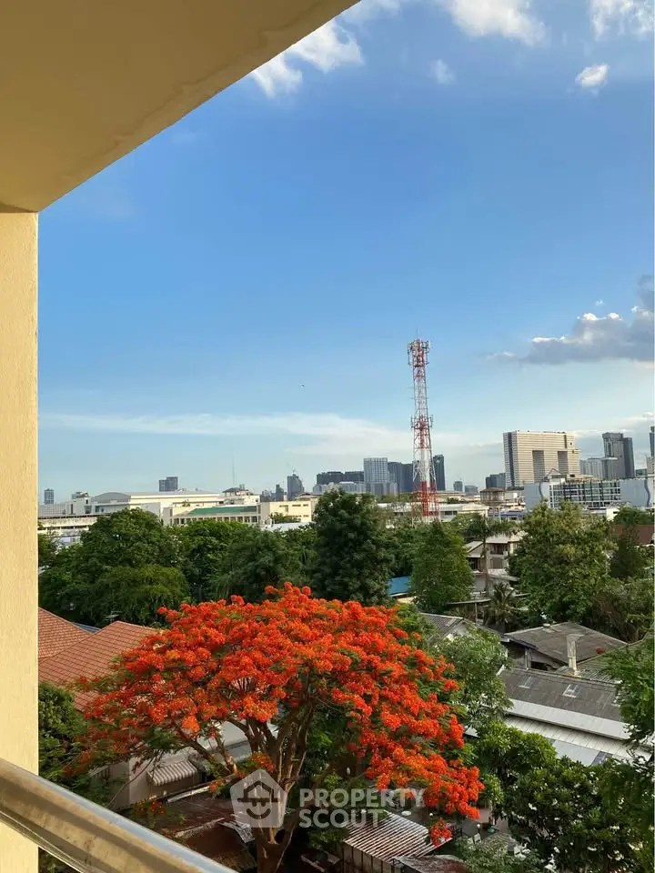 Stunning cityscape view from a balcony with vibrant orange tree and clear blue sky.