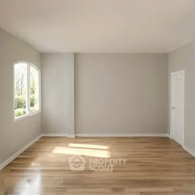 Spacious empty room with wooden flooring and large window offering natural light.