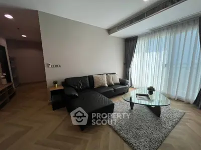 Modern living room with sleek black sofa and glass coffee table, featuring floor-to-ceiling windows.