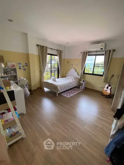 Spacious bedroom with wooden flooring, large window, and cozy decor, perfect for relaxation and comfort.